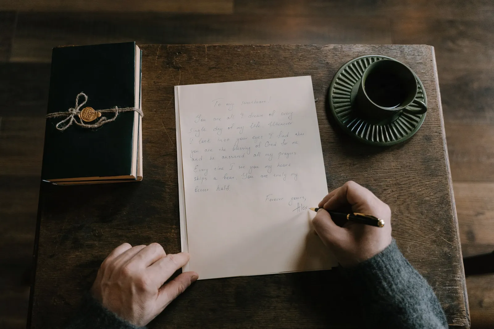 Una carta escrita a mano junto a un cuaderno y un café sobre mesa de madera.