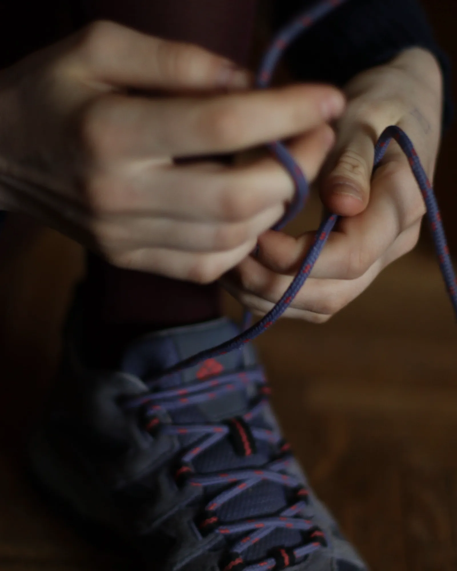 Primer plano de manos atando los cordones de una zapatilla gris y violeta.