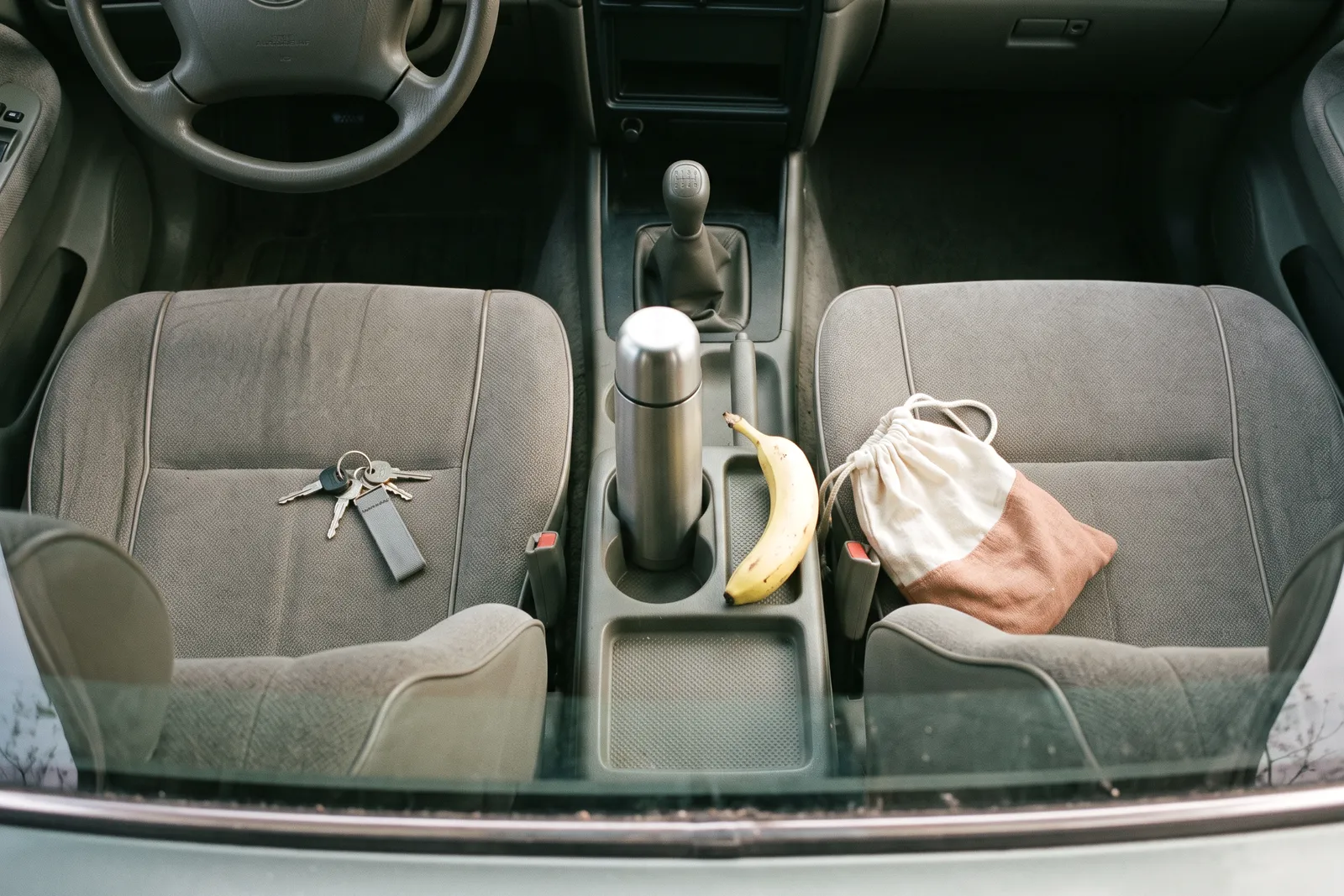 El interior de un auto al amanecer, con un termo en el portavasos, una banana y las llaves sobre el asiento.
