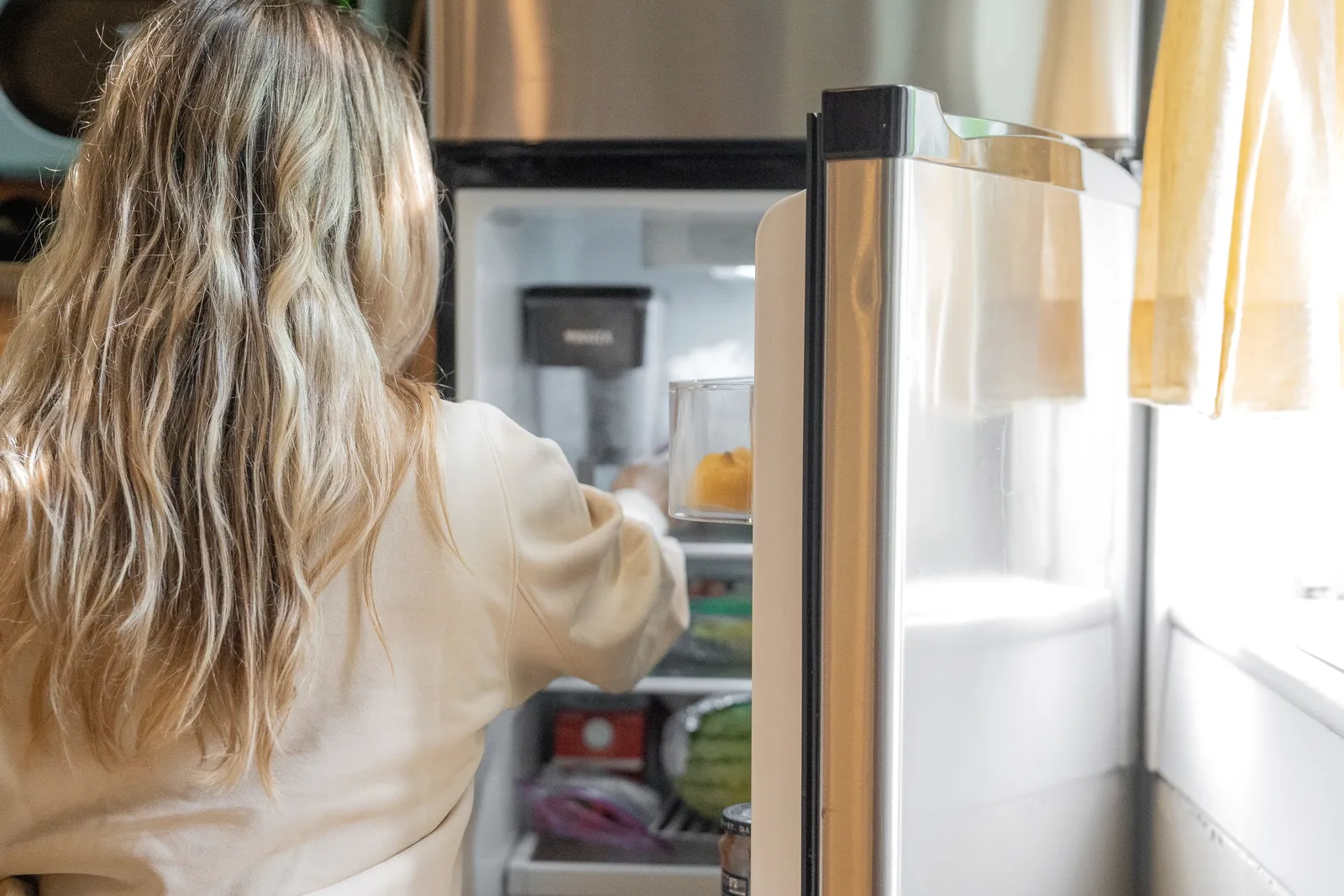 Una persona de espaldas sacando algo del refrigerador en una cocina luminosa.