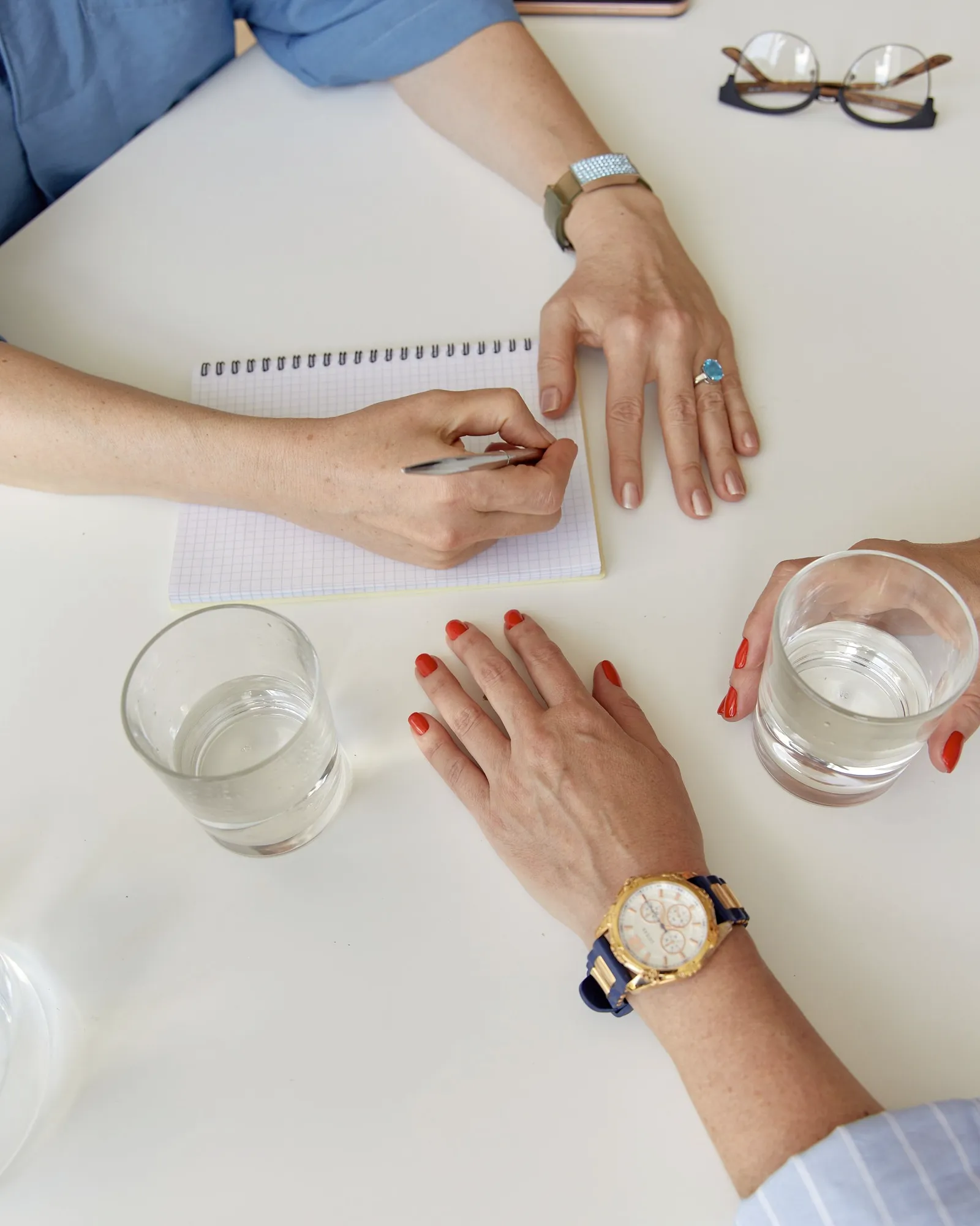 Manos tomando notas y un vaso de agua sobre la mesa, durante una reunion.