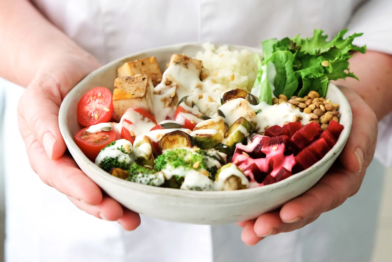 Manos sosteniendo un bol de ensalada de verduras frescas.