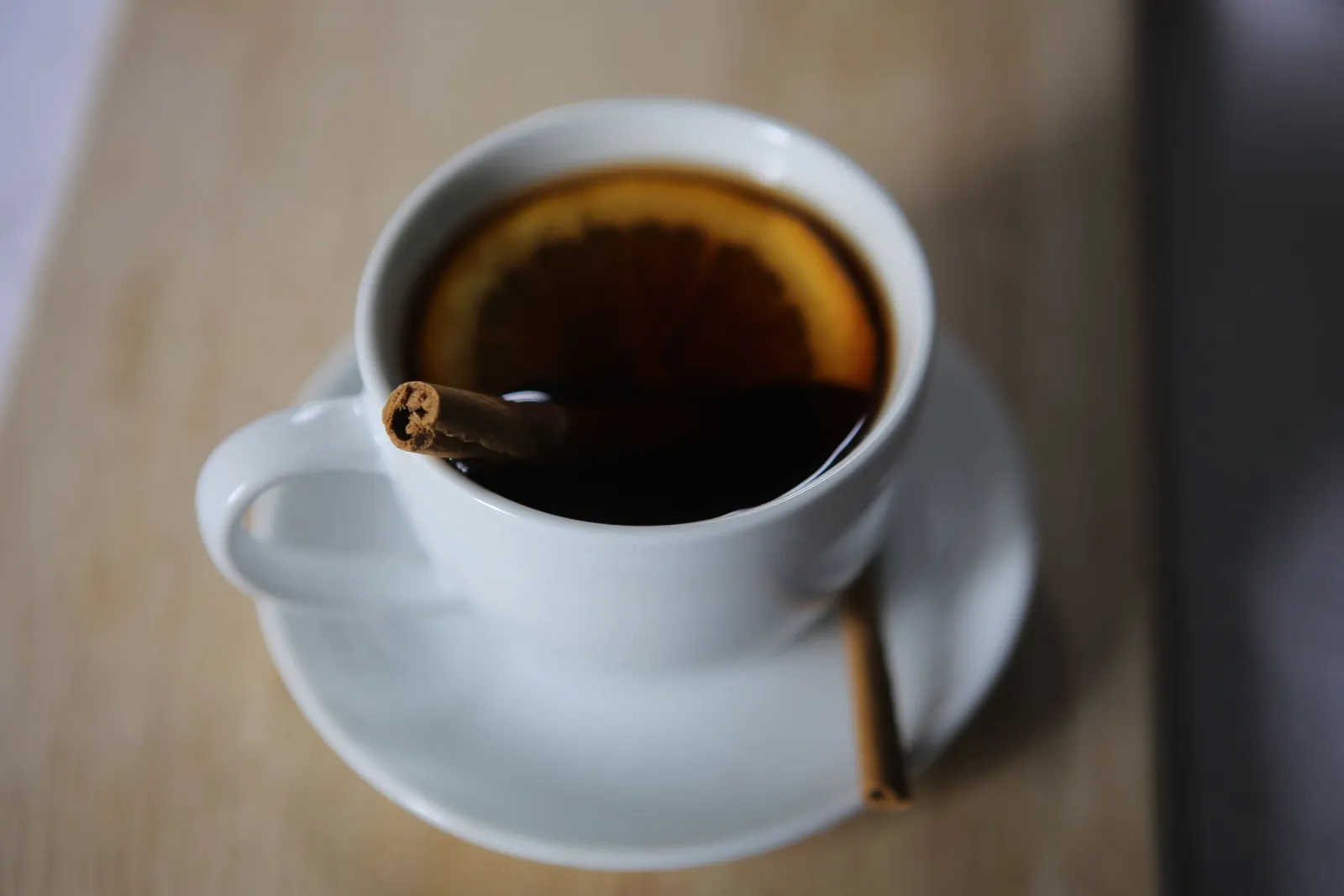 Una taza blanca de té con una rodaja de cítrico y ramas de canela sobre madera.
