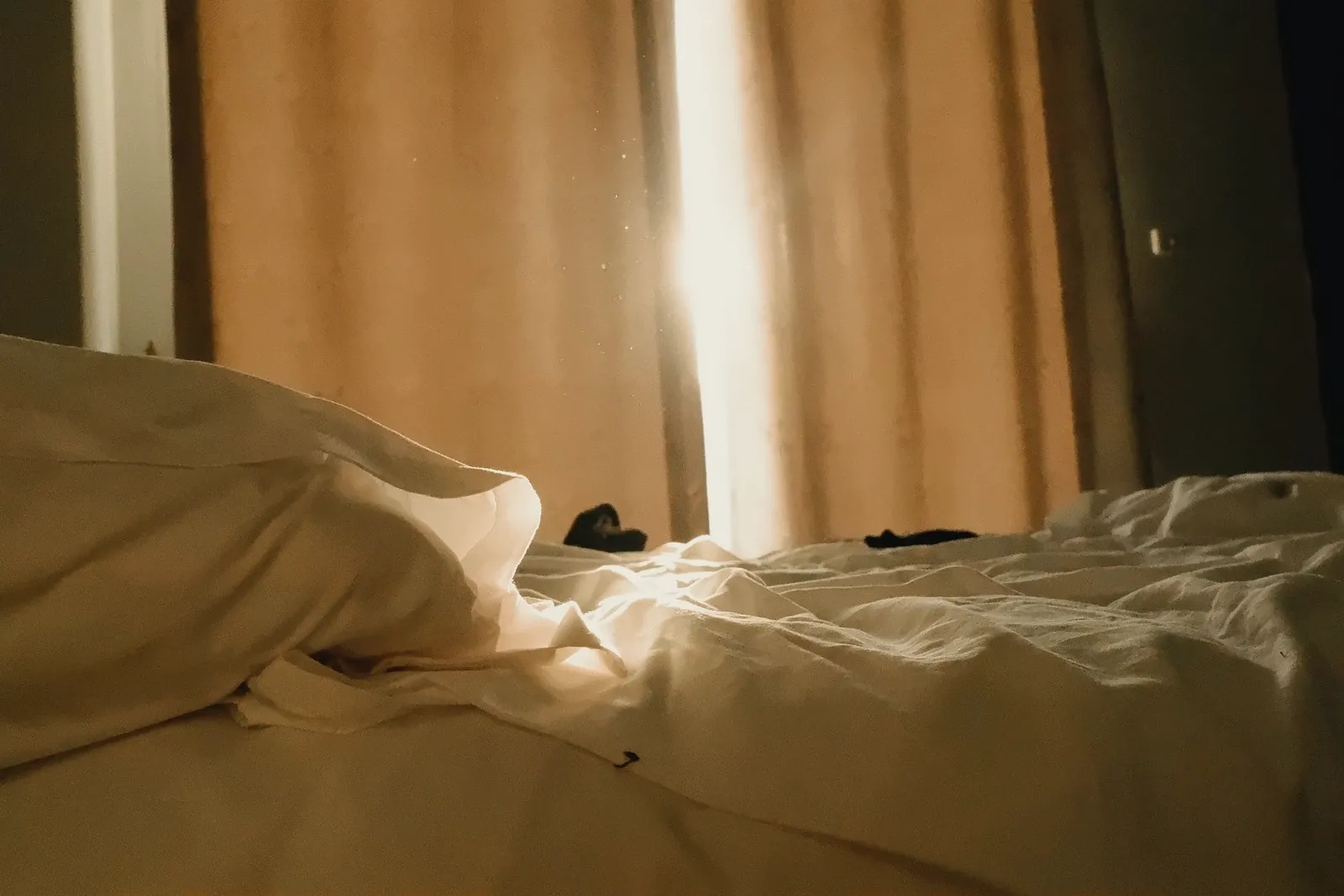 Sol de la mañana entrando por las cortinas sobre una cama sin hacer.