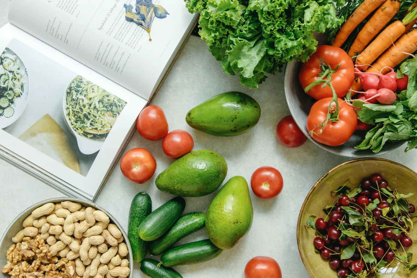 Vista desde arriba de un libro de recetas rodeado de frutas y verduras frescas.