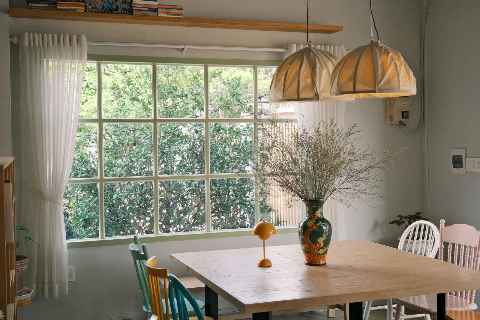 Un comedor luminoso con mesa rústica de madera, sillas dispares y luz natural abundante.