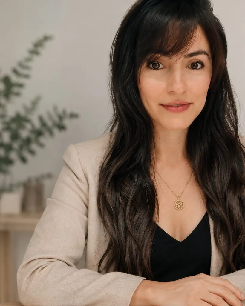 Pamela Altamiranda, coach fisiológica, sentada a una mesa de madera con una planta y una taza, en luz natural