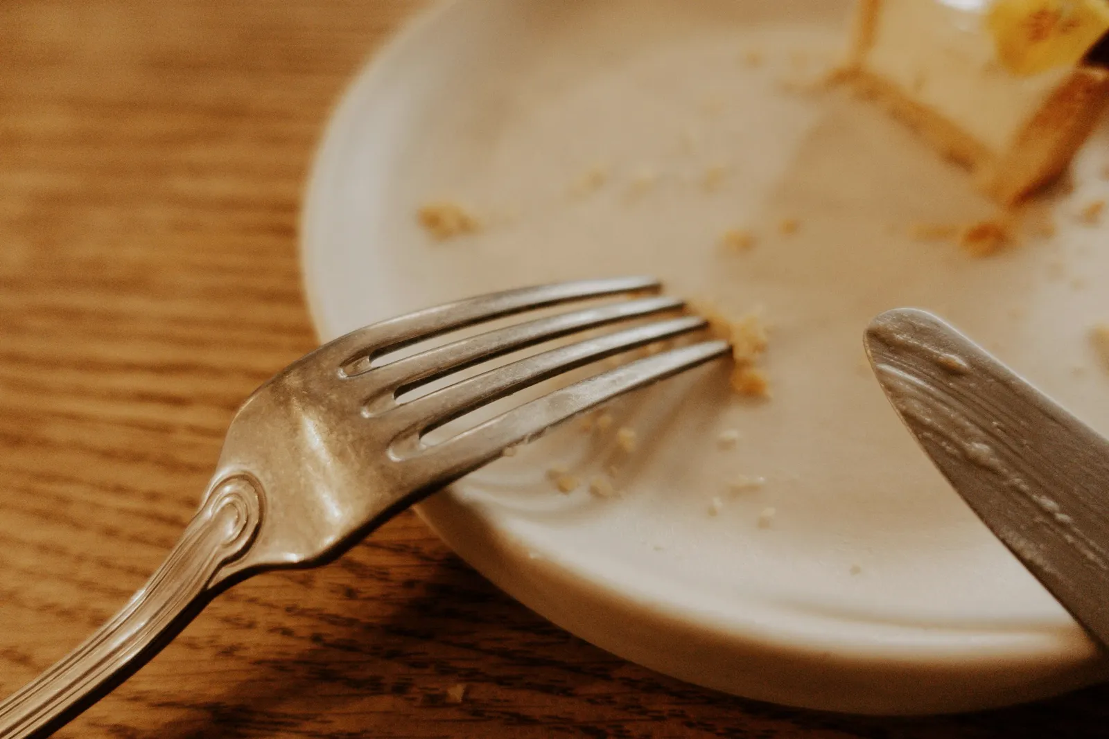 Un tenedor y un cuchillo apoyados en un plato con restos de comida, sobre mesa de madera.