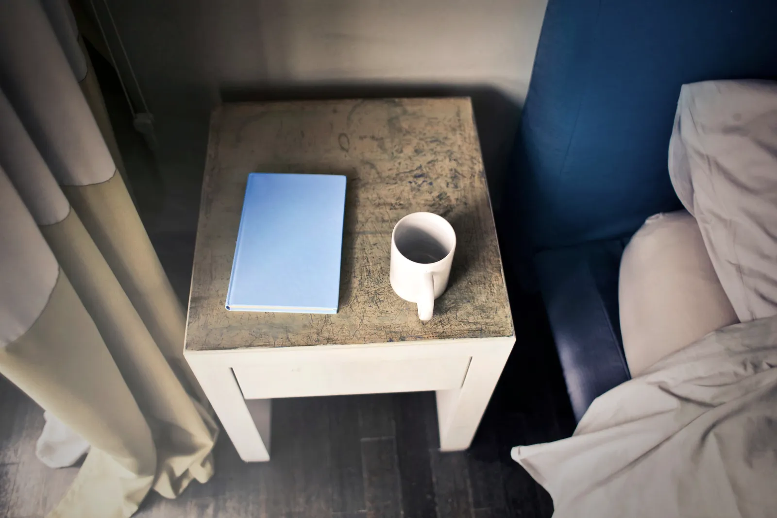 Un libro y una taza sobre una mesa de noche rústica al lado de la cama.