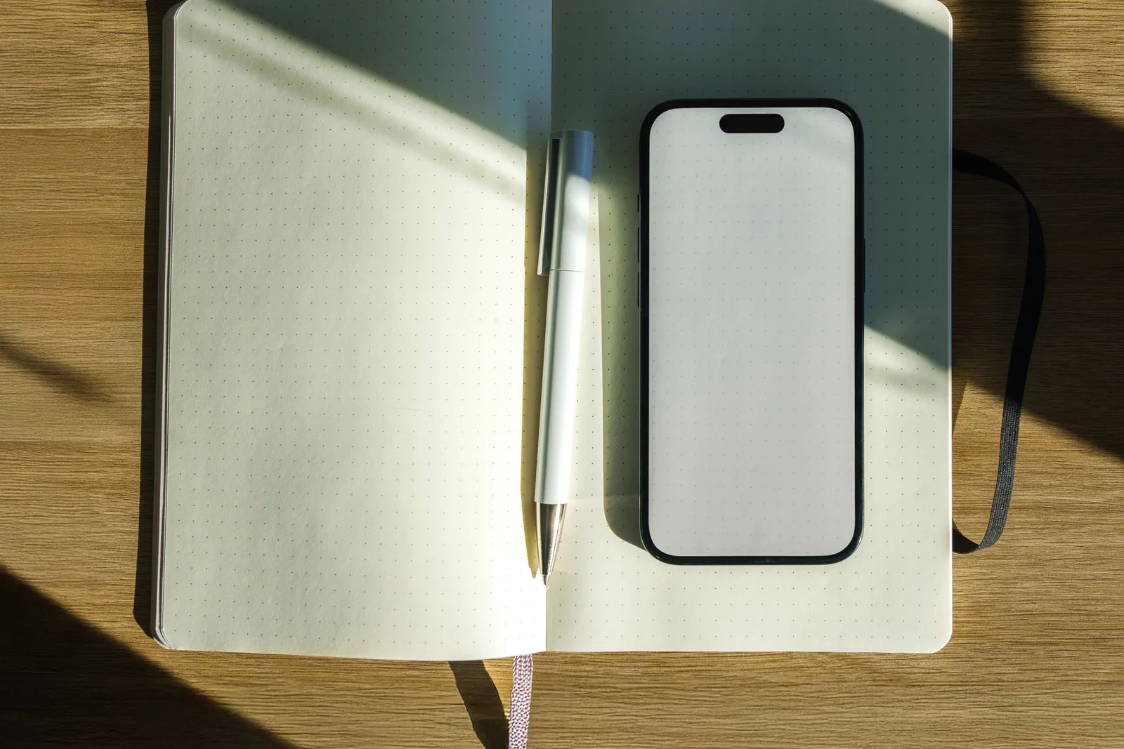 Un escritorio de madera minimalista con un cuaderno abierto, una lapicera y un teléfono al costado.