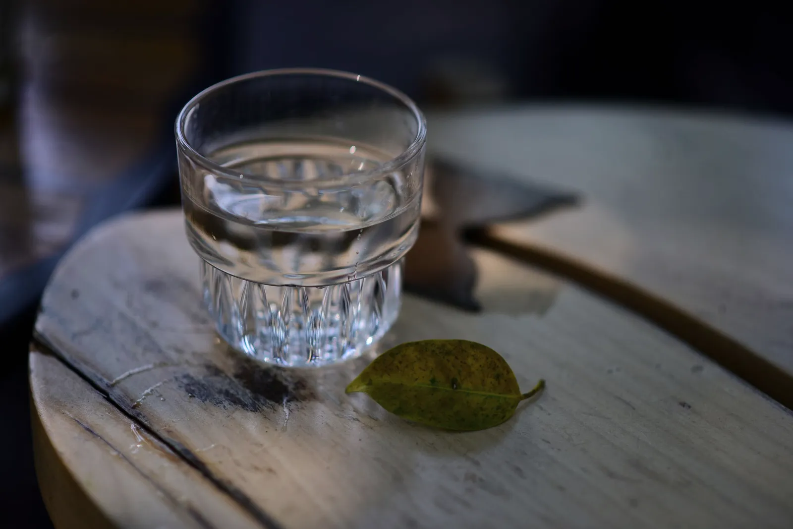 Un vaso de agua clara con una hoja verde al lado, sobre madera rústica.